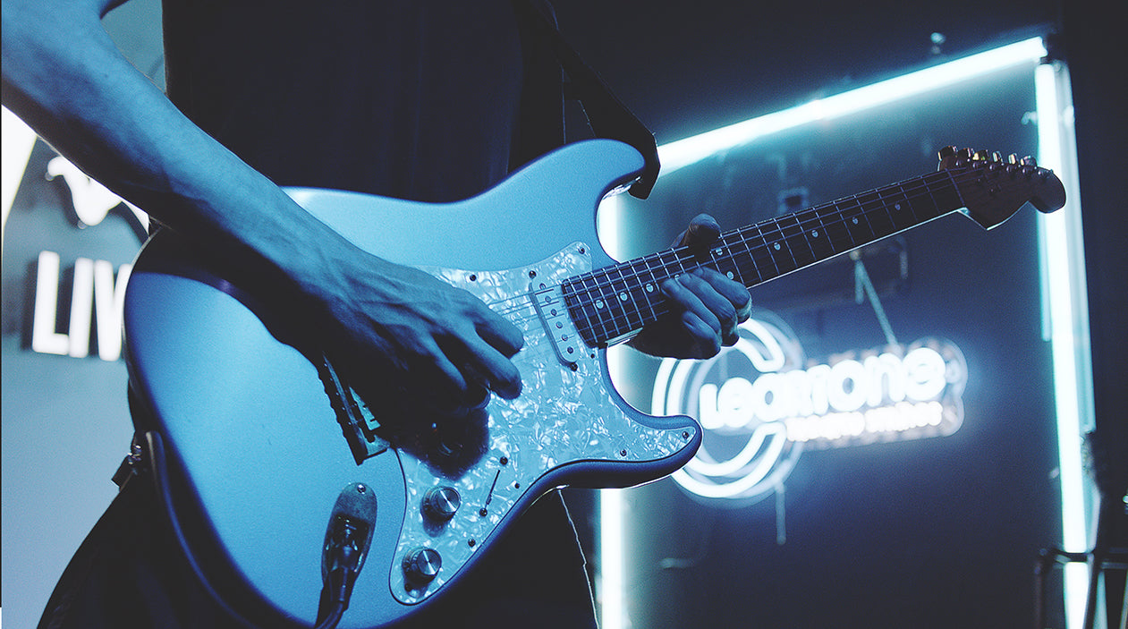 Electric guitar being played onstage in front of a Cleartone Strings logo lit by neon lights